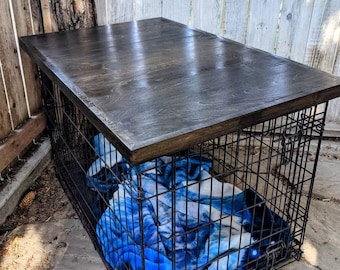 May include: A black metal dog crate with a dark wood top. The crate is sitting on a concrete surface and has a blue blanket inside.