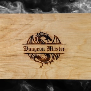 May include: A wooden box with three panels. The center panel has a dragon design with the text "Dungeon Master". The left panel has a dragon design and the right panel has a sword and dice design.