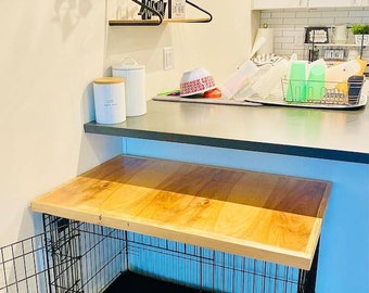 May include: A wooden countertop is attached to a black metal dog crate. The countertop is made of light wood with a natural finish. The crate is made of black metal bars and has a black fabric bed inside. The countertop is about 76 cm long and 30 cm wide.