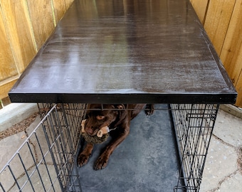 May include: A black metal dog crate with a brown dog inside. The crate has a wooden top and a black mat on the bottom. The dog is lying down and chewing on a toy.