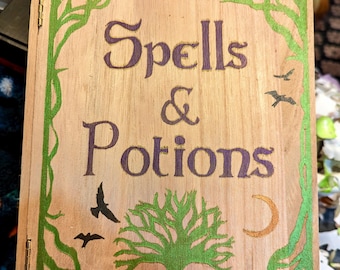 May include: Wooden book cover with the words "Spells & Potions" in purple. The cover is framed with green vines and a tree design, with birds and a crescent moon. The book is made of light-colored wood.