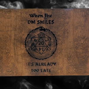 May include: A wooden three-panel tabletop game screen with a black engraved design. The design features a 20-sided die with a snake wrapped around it. The text "When the DM Smiles It's Already Too Late" is also engraved on the screen.
