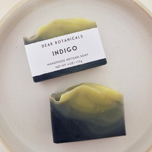 May include: A bar of handmade artisan soap with a black and green swirl design. The soap is labeled "DEAR BOTANICALS INDIGO HANDMADE ARTISAN SOAP NET WT. 4 OZ / 113 G"
