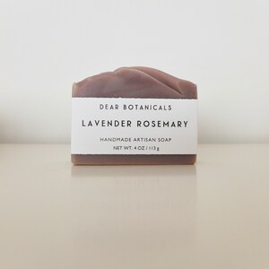 Pu&ograve; includere: Una saponetta rettangolare artigianale fatta a mano con profumo di lavanda e rosmarino. Il sapone &egrave; di colore viola tenue e ha una parte superiore strutturata. Un'etichetta bianca mostra il testo "DEAR BOTANICALS, LAVENDER ROSEMARY, HANDMADE ARTISAN SOAP, NET WT. 4 OZ / 113g."