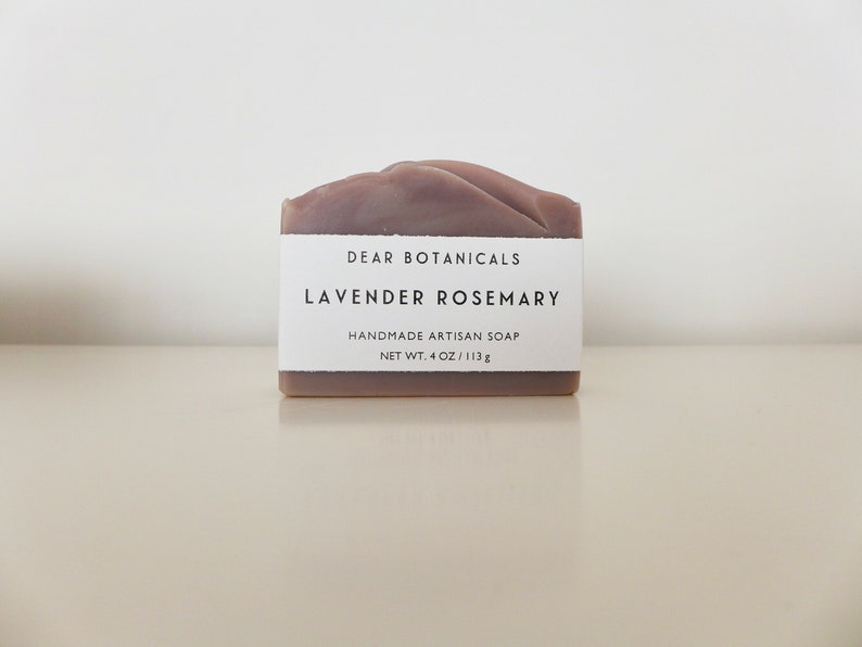 Pu&ograve; includere: Una saponetta rettangolare artigianale fatta a mano con profumo di lavanda e rosmarino. Il sapone &egrave; di colore viola tenue e ha una parte superiore strutturata. Un'etichetta bianca mostra il testo "DEAR BOTANICALS, LAVENDER ROSEMARY, HANDMADE ARTISAN SOAP, NET WT. 4 OZ / 113g."