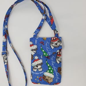 May include: A blue quilted phone pouch with a Christmas dog print. The pouch has a long adjustable strap and features the text "Ho Ho Ho" repeated on the front.