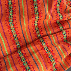 May include: Orange, green, and purple striped fabric with a geometric pattern. The fabric has a white lace trim.