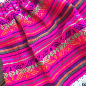 May include: A pink skirt with colorful stripes and a geometric pattern. The skirt has a white lace trim.