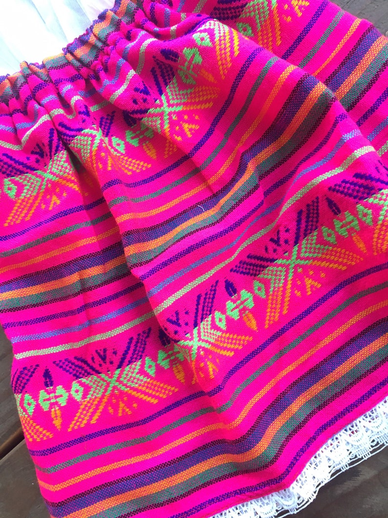 May include: A pink skirt with colorful stripes and a geometric pattern. The skirt has a white lace trim.