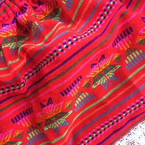 May include: Red skirt with colorful embroidered flowers and geometric patterns. The skirt has a white lace trim.