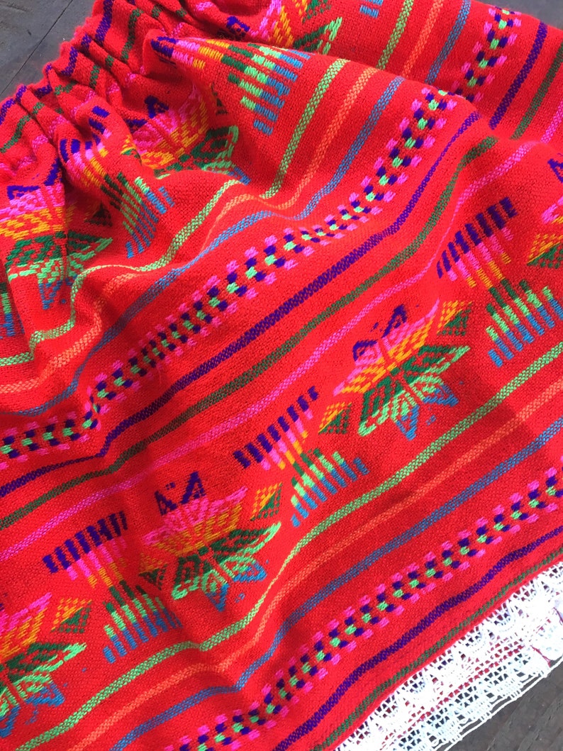May include: Red skirt with colorful embroidered flowers and geometric patterns. The skirt has a white lace trim.