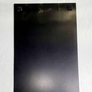 May include: A black rectangular metal plate with two white electrical outlets on the bottom.