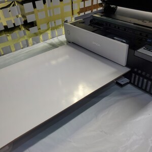 May include: A white printer with the word "EPSON" printed on the front. A white rectangular piece of paper is being fed into the printer.