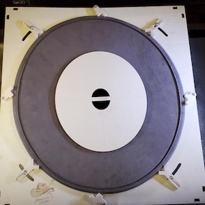 May include: A circular drum head with a gray outer ring and a white inner circle. The center has a black horizontal oval. The drum head is secured to a wooden frame with white clips. The text "Showcase Drums" is visible in the lower left corner.