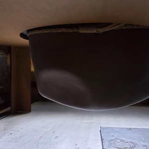 May include: A dark, bowl-shaped object suspended from a wooden surface. The object appears to be made of a dark material, possibly metal or a composite. The image is taken from a low angle, looking up.