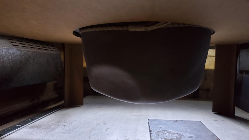 May include: A dark, bowl-shaped object suspended from a wooden surface. The object appears to be made of a dark material, possibly metal or a composite. The image is taken from a low angle, looking up.