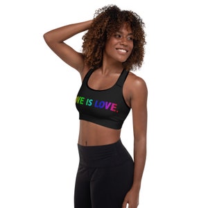May include: A black sports bra with a rainbow "LOVE IS LOVE." graphic. The model is wearing black leggings.
