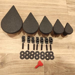 May include: A set of eight black teardrop-shaped knobs with eight matching black screws and eight black washers. The knobs are arranged in a row from largest to smallest.