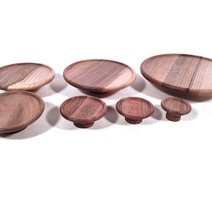 May include: Set of seven wooden knobs in various sizes, all made from walnut wood. The knobs are round and have a smooth, polished finish.