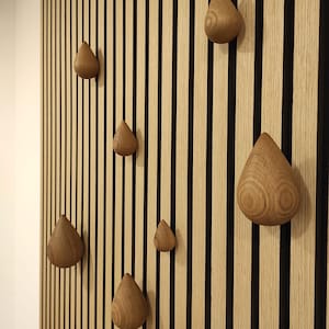 May include: A wall with vertical wooden slats in a light brown color with black vertical slats interspersed. There are seven wooden teardrop-shaped hooks attached to the wall.