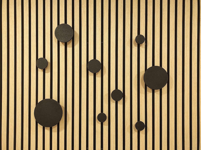 Puede incluir: Un panel de pared de madera con rayas negras verticales y vetas de madera de color marr&oacute;n claro. Varios ganchos de pared negros y circulares de diferentes tama&ntilde;os est&aacute;n adheridos al panel, creando un dise&ntilde;o decorativo y funcional.