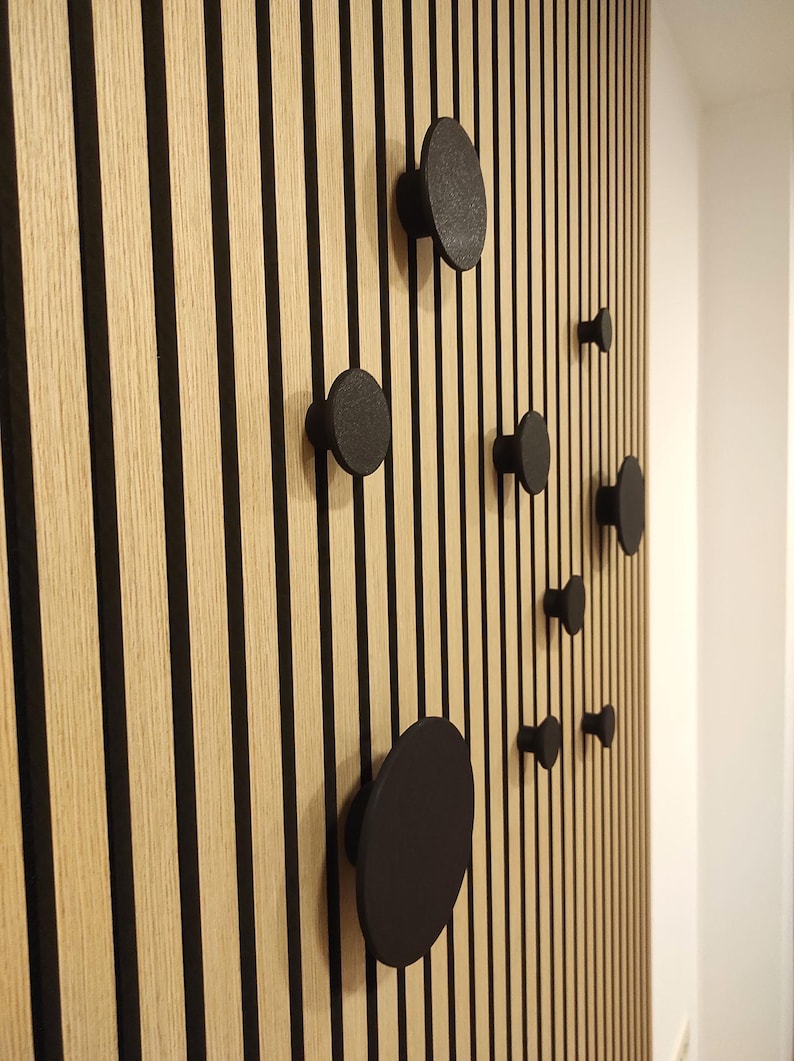 Puede incluir: Un panel de pared de madera con rayas negras verticales y varios ganchos de pared negros y redondos de diferentes tama&ntilde;os. Los ganchos est&aacute;n espaciados uniformemente, creando un dise&ntilde;o moderno.