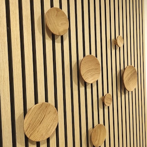 May include: A wall with vertical wooden slats in a light brown color with black lines between each slat. There are six round wooden knobs of varying sizes attached to the wall.
