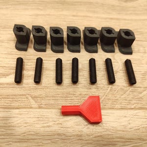 Puede incluir: Un conjunto de componentes de pl&aacute;stico negro, que incluye ocho piezas anguladas y seis tornillos, dispuestos sobre una superficie de madera. Tambi&eacute;n se incluye una herramienta roja. Los art&iacute;culos parecen ser hardware o piezas para un ensamblaje m&aacute;s grande.