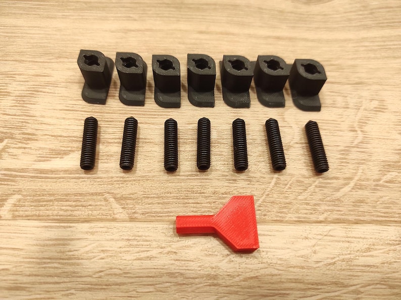 Puede incluir: Un conjunto de componentes de pl&aacute;stico negro, que incluye ocho piezas anguladas y seis tornillos, dispuestos sobre una superficie de madera. Tambi&eacute;n se incluye una herramienta roja. Los art&iacute;culos parecen ser hardware o piezas para un ensamblaje m&aacute;s grande.
