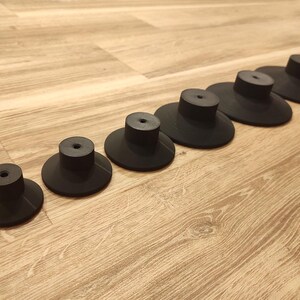 Puede incluir: Un conjunto de siete pomos de armario negros con una base circular plana y un v&aacute;stago cil&iacute;ndrico. Los pomos est&aacute;n dispuestos en diagonal sobre una superficie de madera marr&oacute;n claro.