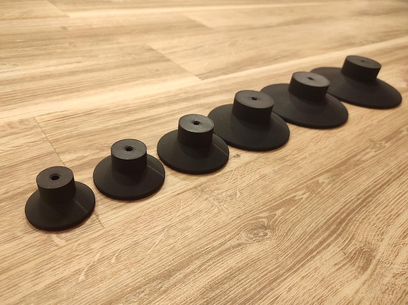 Puede incluir: Un conjunto de siete pomos de armario negros con una base circular plana y un v&aacute;stago cil&iacute;ndrico. Los pomos est&aacute;n dispuestos en diagonal sobre una superficie de madera marr&oacute;n claro.