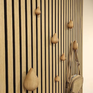 Può includere: Un muro con listelli di legno di colore marrone chiaro con linee nere che corrono verticalmente. Ci sono sei ganci di legno a forma di goccia, e una borsa di pelle marrone è appesa a uno dei ganci.
