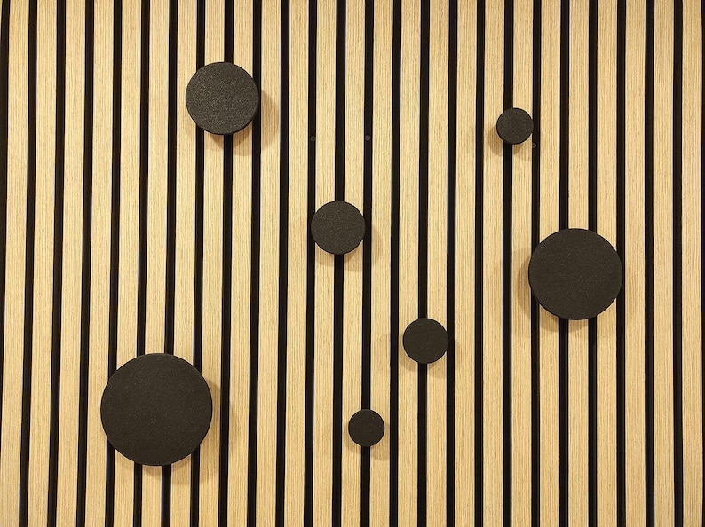 Puede incluir: Un panel de pared de madera con listones verticales de madera de color claro y rayas negras. Varias decoraciones de pared circulares negras est&aacute;n fijadas al panel, creando un dise&ntilde;o moderno y minimalista.