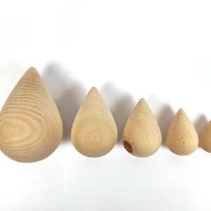 Puede incluir: Cinco objetos de madera en forma de lágrima de diferentes tamaños, dispuestos de mayor a menor. Las lágrimas están hechas de madera de color claro, mostrando los patrones naturales de la veta. Los objetos están sobre un fondo blanco.