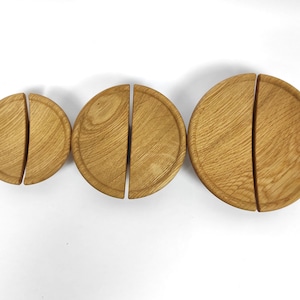 May include: Three wooden round serving platters, each split into two semi-circles. The platters are made of light brown wood with visible grain patterns. The sizes vary, with the largest platter measuring approximately 8 inches in diameter.