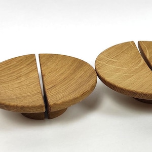 May include: Close-up of several wooden cabinet knobs. Each knob is a light brown colour, with a semi-circular shape split into two halves. The knobs have a natural wood grain pattern and are mounted on a small, round base.