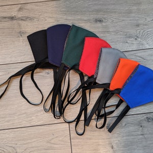 May include: A set of eight face masks in various colors, including black, navy blue, green, red, gray, orange, and blue. The masks are made of fabric and have black ties.