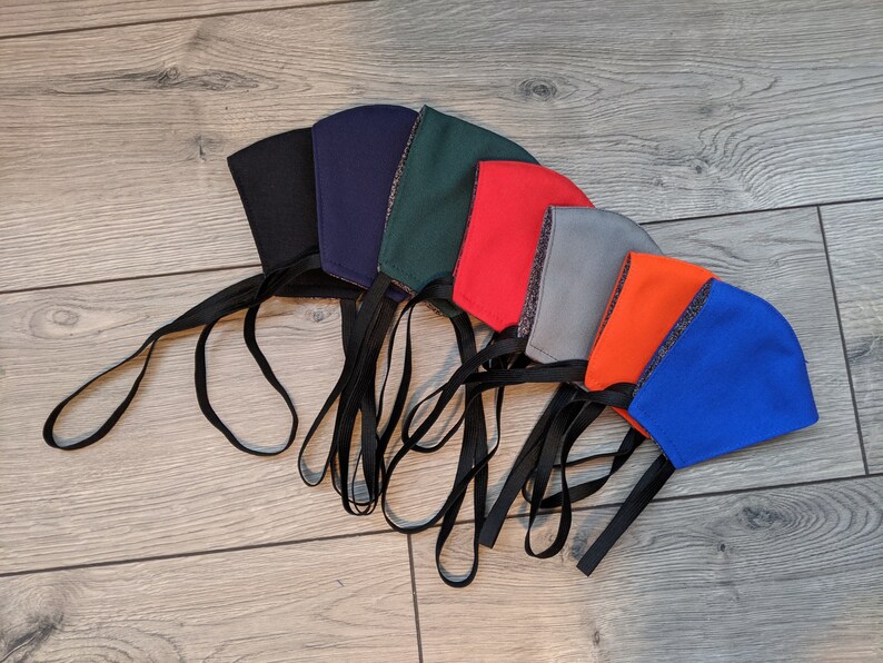 May include: A set of eight face masks in various colors, including black, navy blue, green, red, gray, orange, and blue. The masks are made of fabric and have black ties.