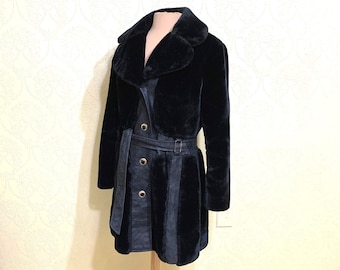 May include: A black faux fur coat with a wide collar and a belted waist. The coat features a vertical panel design on the lower half and is displayed on a mannequin. The coat has gold-colored buttons and a matching belt with a gold buckle.