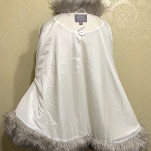 May include: White faux fur trimmed cape with a button closure. The label reads "Jessica London".