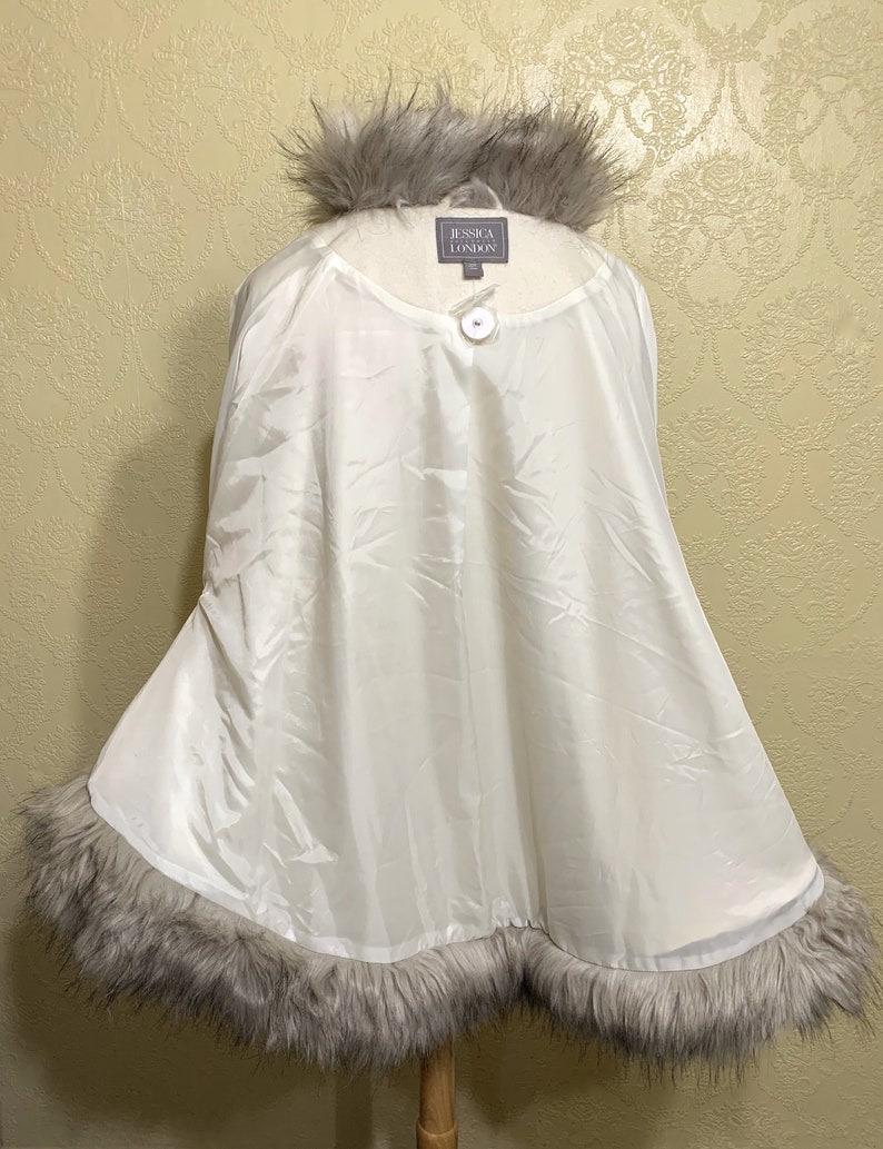 May include: White faux fur trimmed cape with a button closure. The label reads "Jessica London".