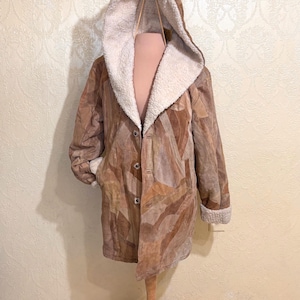 May include: A brown patchwork coat with a hood and a cream-colored fleece lining. The coat has a button-up front and is displayed on a wooden mannequin. The coat's sleeves have fleece cuffs.