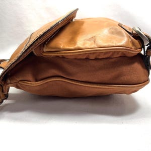 Pu&ograve; includere: Una borsa a tracolla marrone con chiusura a patta. La borsa presenta una combinazione di pelle e tela. La pelle &egrave; di colore marrone chiaro e la tela &egrave; di un marrone pi&ugrave; scuro. La borsa ha una fibbia argentata e una lunga tracolla.