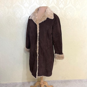 May include: A long brown suede coat with a faux fur collar and cuffs. The coat has a button closure and a single pocket on the left side.