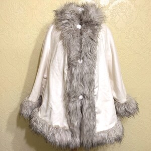 May include: A white faux fur cape with a gray fur trim around the collar, hem, and down the front. The cape has white buttons down the front.