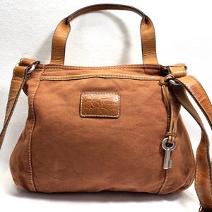 Pu&ograve; includere: Borsa a tracolla Fossil marrone con manico superiore e tracolla regolabile. La borsa presenta un ciondolo a forma di chiave e una toppa in pelle con il logo Fossil. La borsa &egrave; realizzata in materiale simile alla tela.