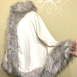 May include: A white faux fur shawl with a gray faux fur trim around the collar and hem.
