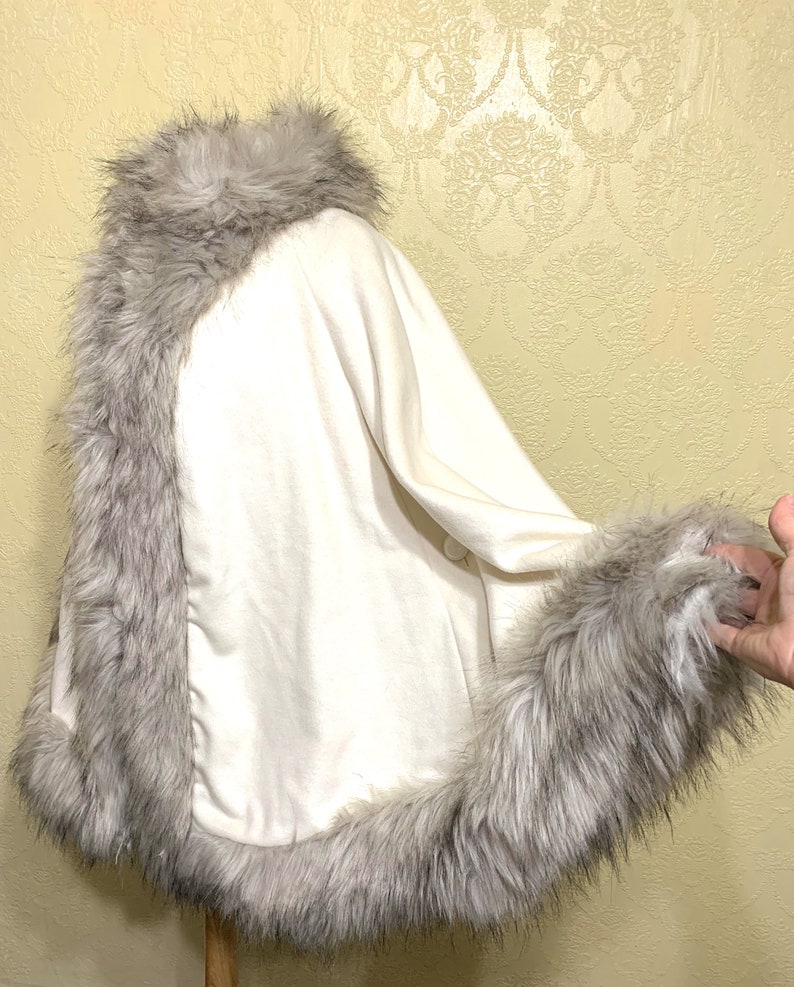 May include: A white faux fur shawl with a gray faux fur trim around the collar and hem.