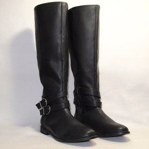 May include: A pair of black leather knee-high boots with silver buckles. The boots have a pointed toe and a low heel.