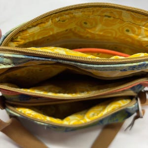 Pu&ograve; includere: Borsa a tracolla multi-scomparto con un motivo floreale nei toni del blu, verde e arancione. La borsa ha una tracolla regolabile marrone e cerniere color oro. La fodera interna &egrave; gialla con un design floreale.